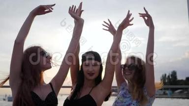 快乐最好的女朋友在日落时在海滩上跳舞，三个女人在海边举起手臂，夏天的晚上